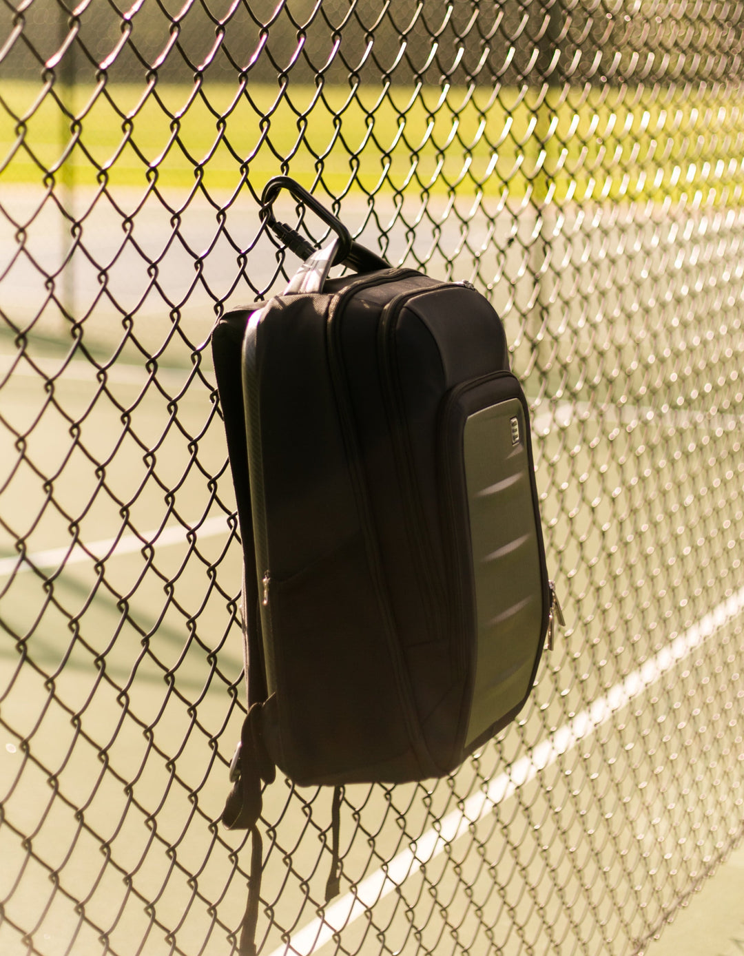 Ethos Pickleball backpack hanging on a chain-link fence with a tennis court in the background