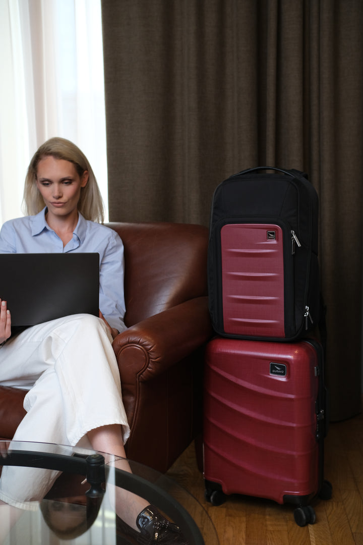 Duravo red carry-on and red backpack on a wooden floor with a person sitting on a chair holding a black folder.