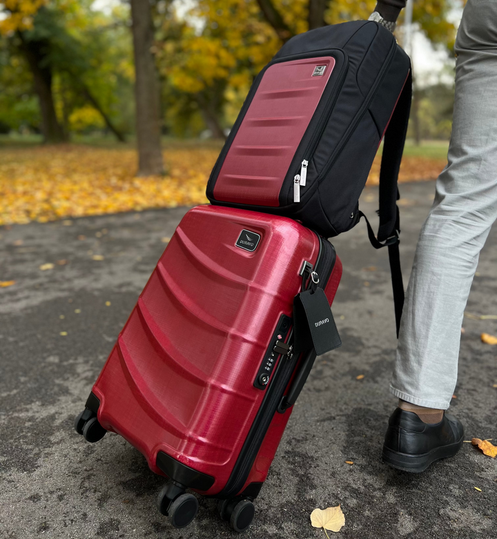 Duravo Red carry-on and red/black backpack on a pavement with trees in the background